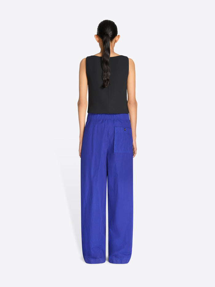 Back view of a model stands against a light gray background wearing a sleeveless top with a multicolor pixelated pattern and a gold textured waistband, paired with wide-leg royal blue pants.
