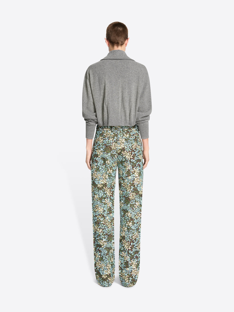 Back view of a model standing against a light gray background wearing a gray knit cardigan paired with high-waisted floral patterned trousers.