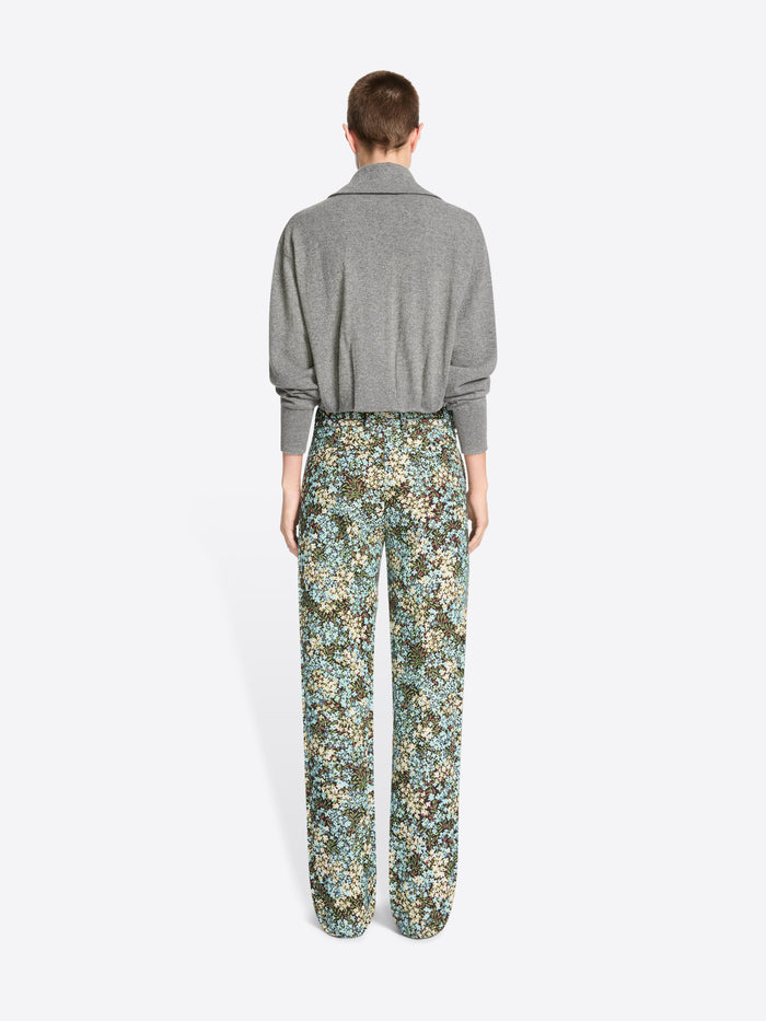 Back view of a model standing against a light gray background wearing a gray knit cardigan paired with high-waisted floral patterned trousers.