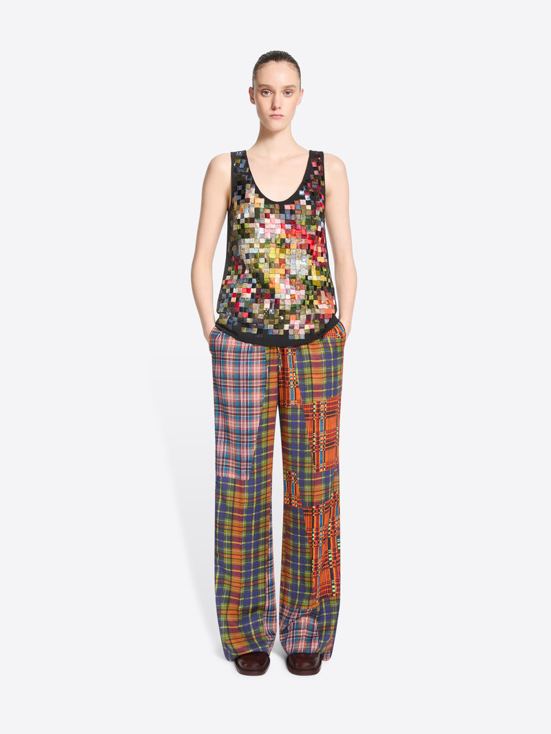 A model stands against a light gray background wearing a tank top with a colorful pixelated pattern and matching wide-leg plaid pants with vertical patchwork panels.