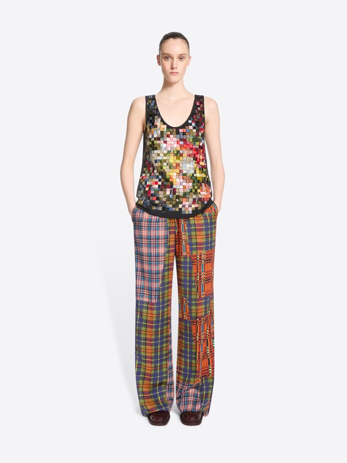 A model stands against a light gray background wearing a tank top with a colorful pixelated pattern and matching wide-leg plaid pants with vertical patchwork panels.