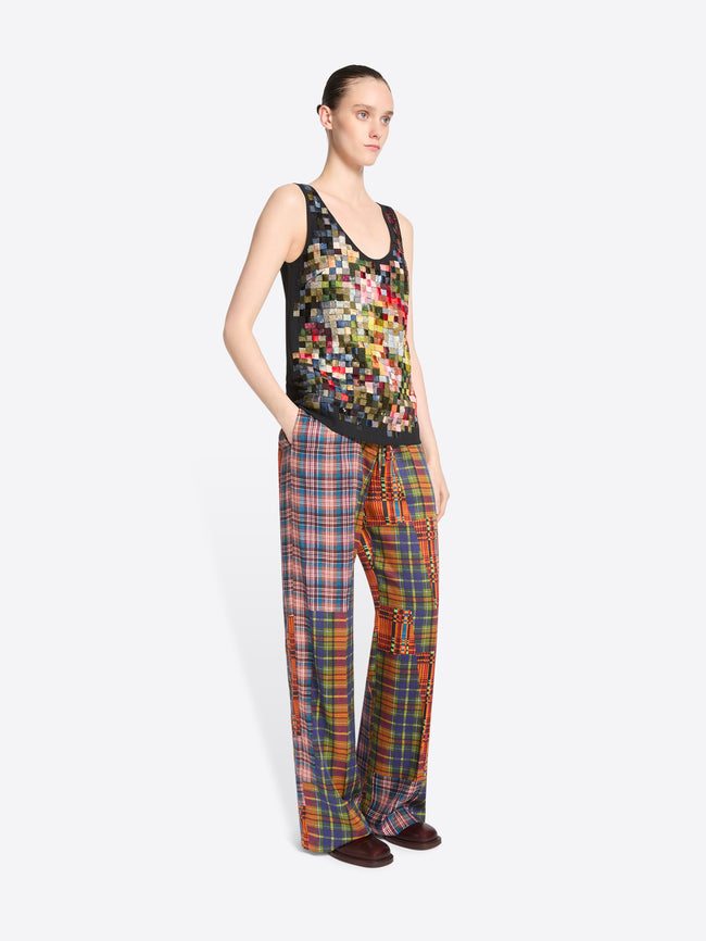 A model stands against a light gray background wearing a tank top with a colorful pixelated pattern and matching wide-leg plaid pants with vertical patchwork panels.