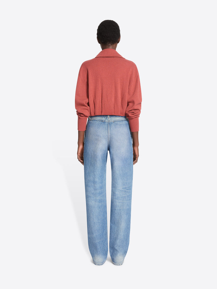 Back view of a model stands against a light gray background wearing a long-sleeve coral cardigan, paired with light-wash wide-leg jeans.