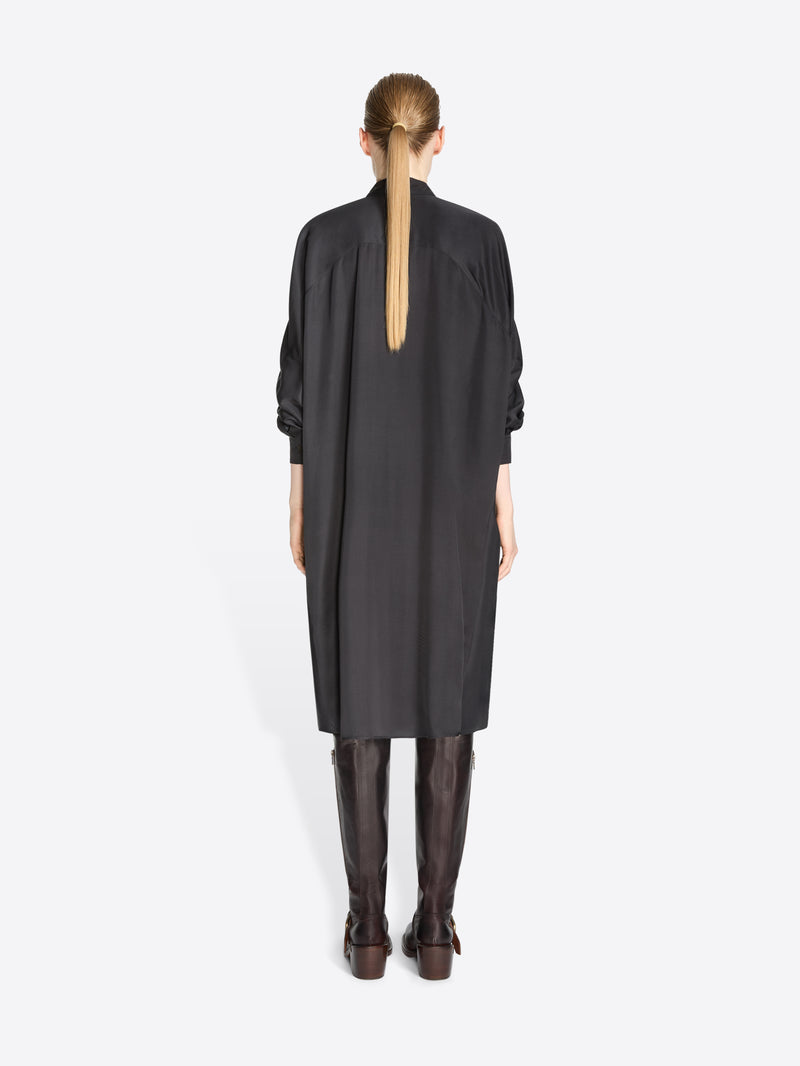 A back view of a model standing against a light gray background wearing a black long-sleeve shirt dress paired with dark brown knee-high boots.