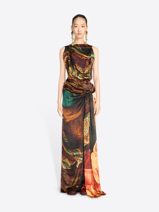 A model wearing a sleeveless, floor-length draped gown with an abstract painterly print, set against a light gray background.