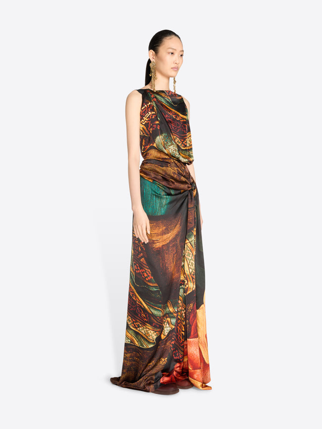 A model wearing a sleeveless, floor-length draped gown with an abstract painterly print, set against a light gray background.