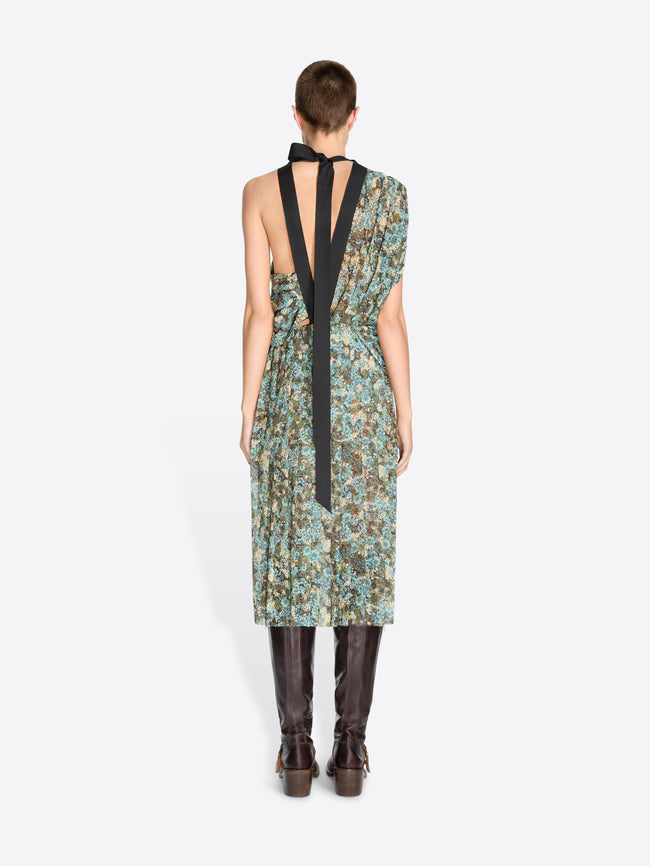 Back view of a model standing against a light gray background wearing a sleeveless, one-shoulder midi dress with a green and blue floral print, paired with dark brown knee-high boots.