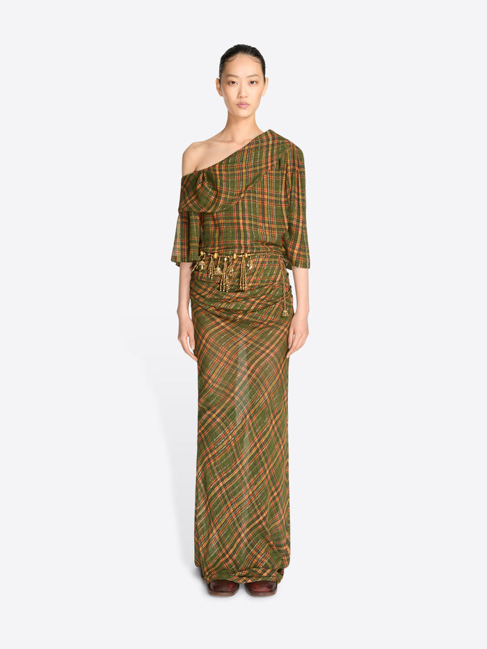 A model wearing a long, one-shoulder dress with a green and brown plaid pattern and gold tassel detailing at the waist, set against a light gray background.