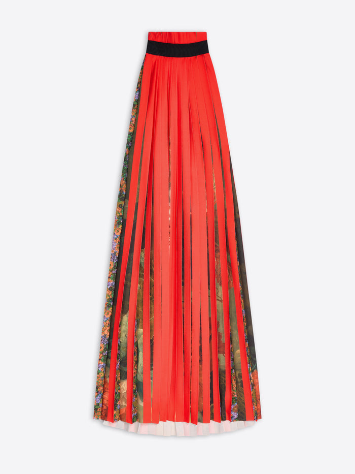 A long pleated dress in bright red-orange with a black collar and vertical panels of multicolor floral and botanical print, shown on a light gray background.