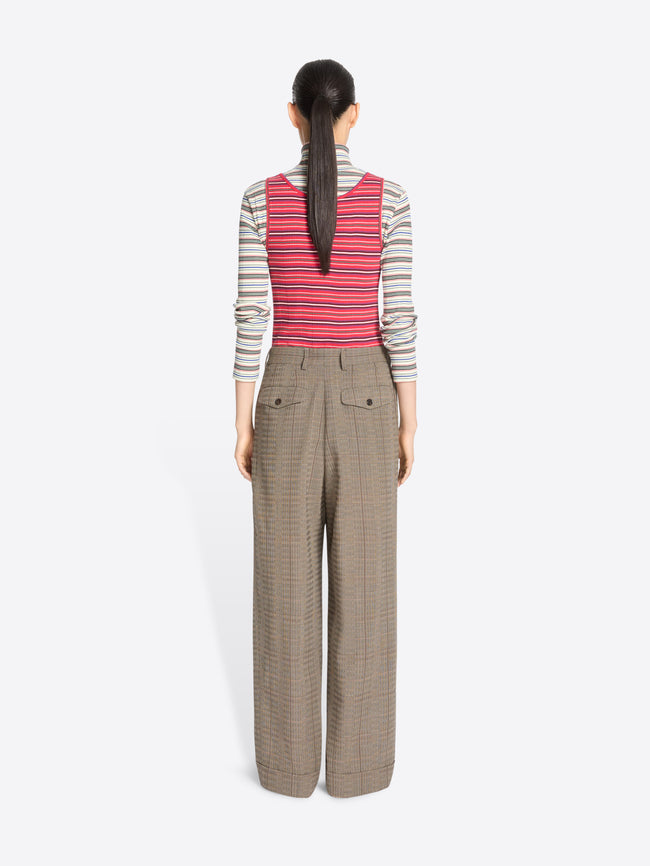 A back view of a model standing against a light gray background wearing a striped turtleneck top, a striped tank top, wide-leg pleated pants, and snakeskin shoes.