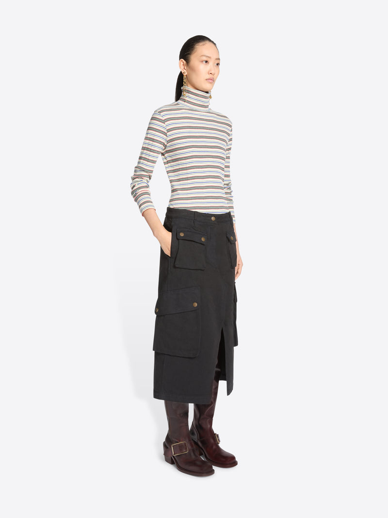 A model stands against a light gray background wearing a striped turtleneck sweater, a black cargo midi skirt with front flap pocket and dark brown knee-high boots.