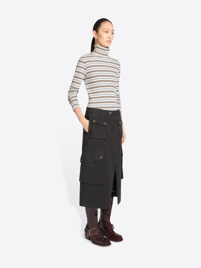 A model stands against a light gray background wearing a striped turtleneck sweater, a black cargo midi skirt with front flap pocket and dark brown knee-high boots.