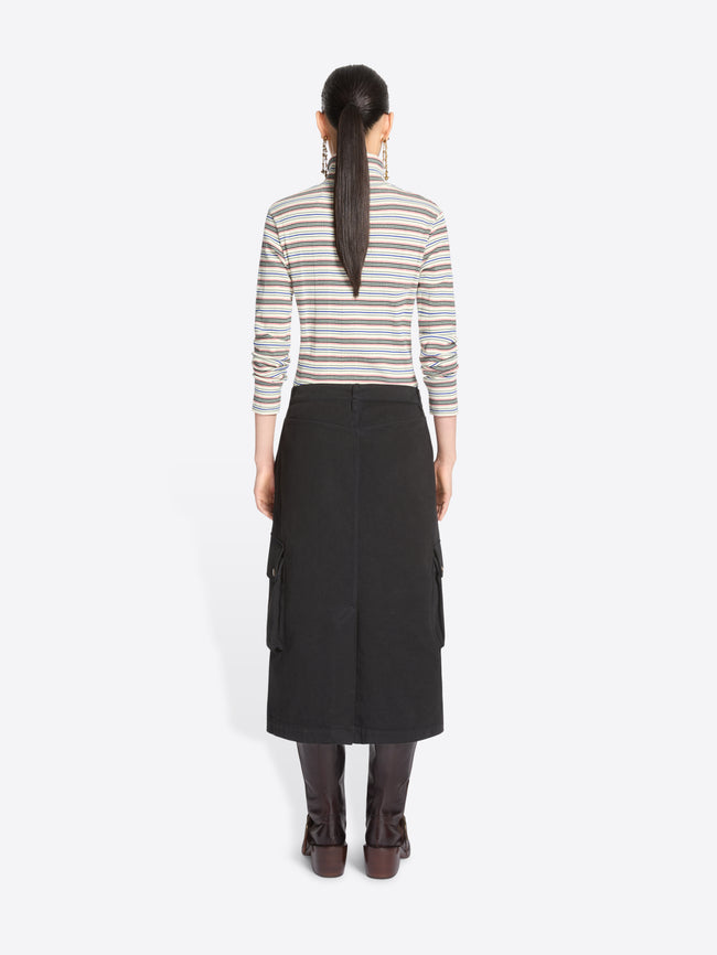 Back view of a model standing against a light gray background wearing a striped turtleneck sweater, a black cargo midi skirt with front flap pocket and dark brown knee-high boots.