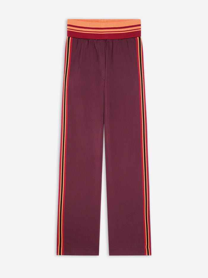 A pair of wide-leg pants in maroon, featuring double vertical stripes in yellow and orange running down the sides, with a matching red and orange striped elastic waistband.