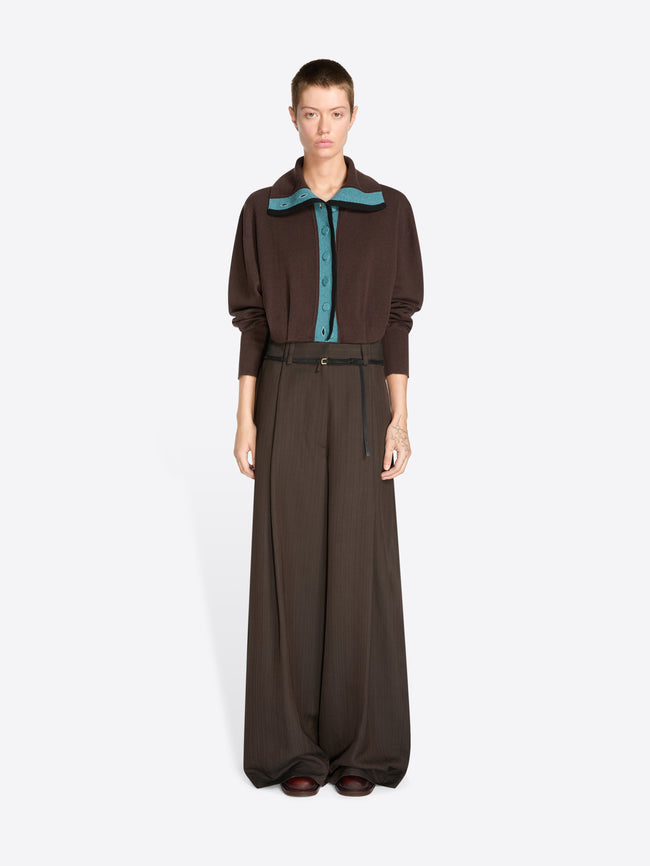 A model stands against a light gray background wearing a dark brown long-sleeve collared cardigan with a teal inner placket and matching wide-leg trousers with a thin waist belt.