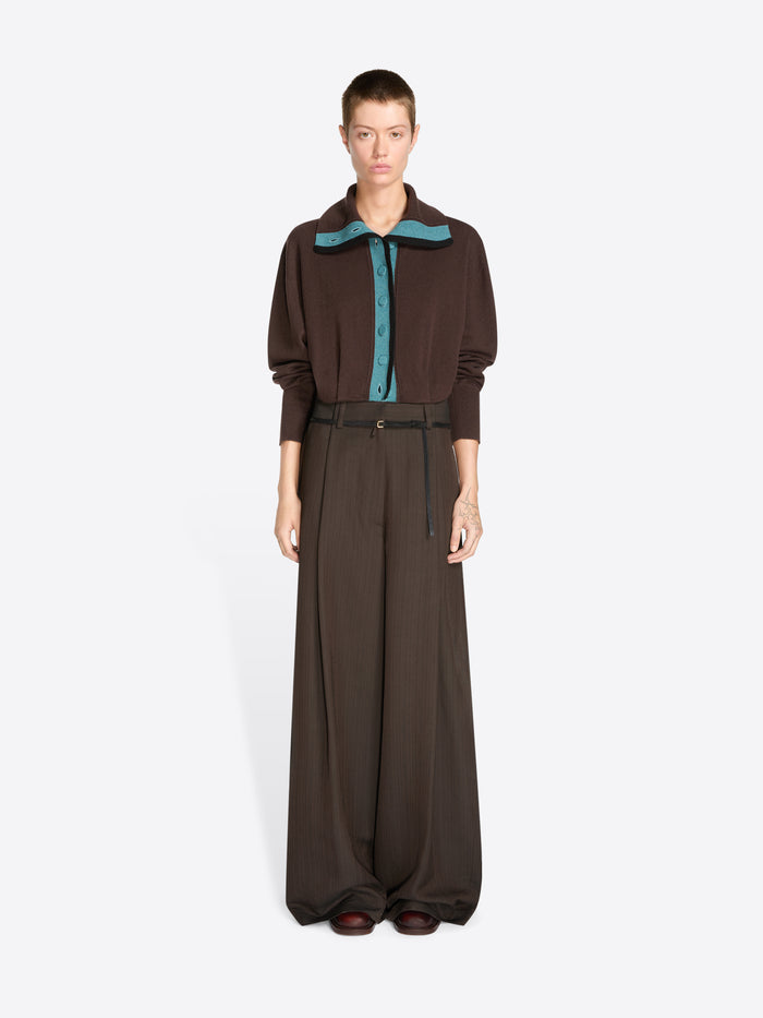 A model stands against a light gray background wearing a dark brown long-sleeve collared cardigan with a teal inner placket and matching wide-leg trousers with a thin waist belt.