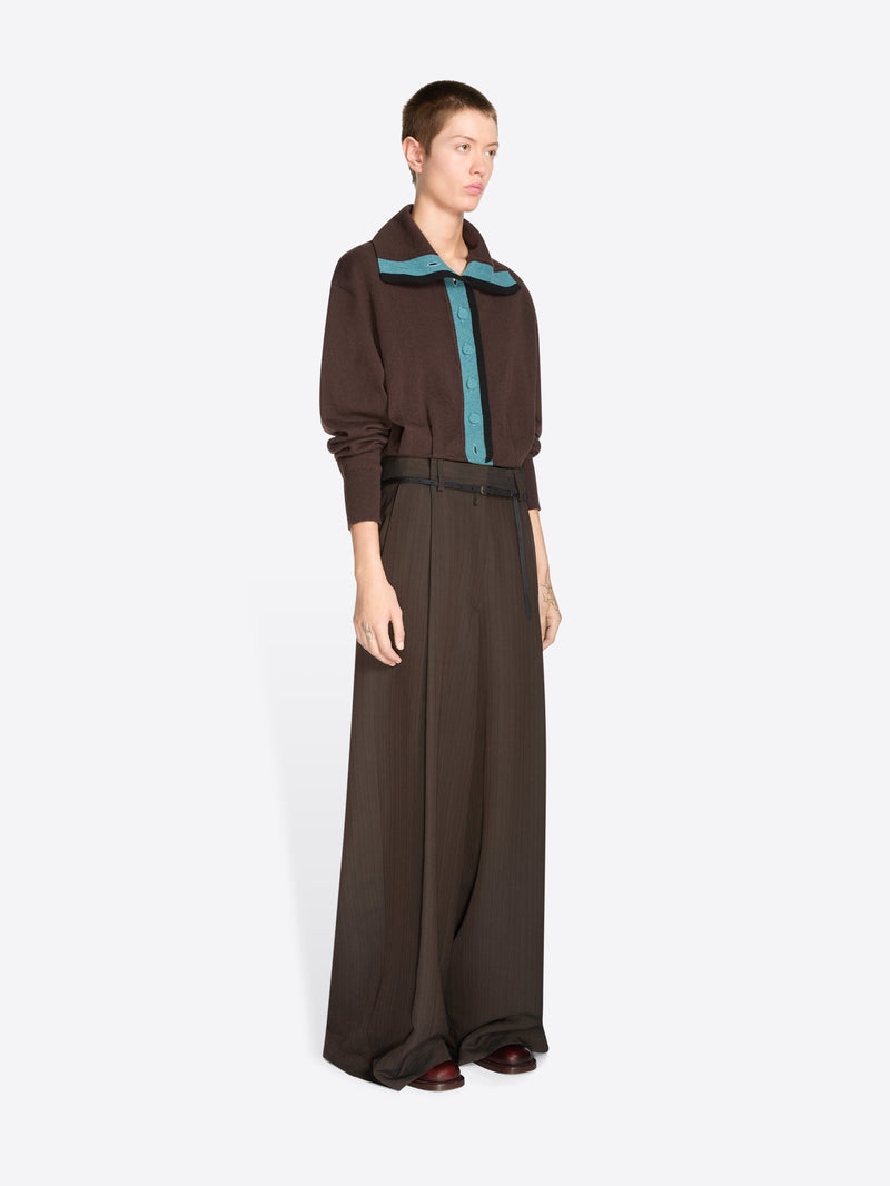 A model stands against a light gray background wearing a dark brown long-sleeve collared cardigan with a teal inner placket and matching wide-leg trousers with a thin waist belt.