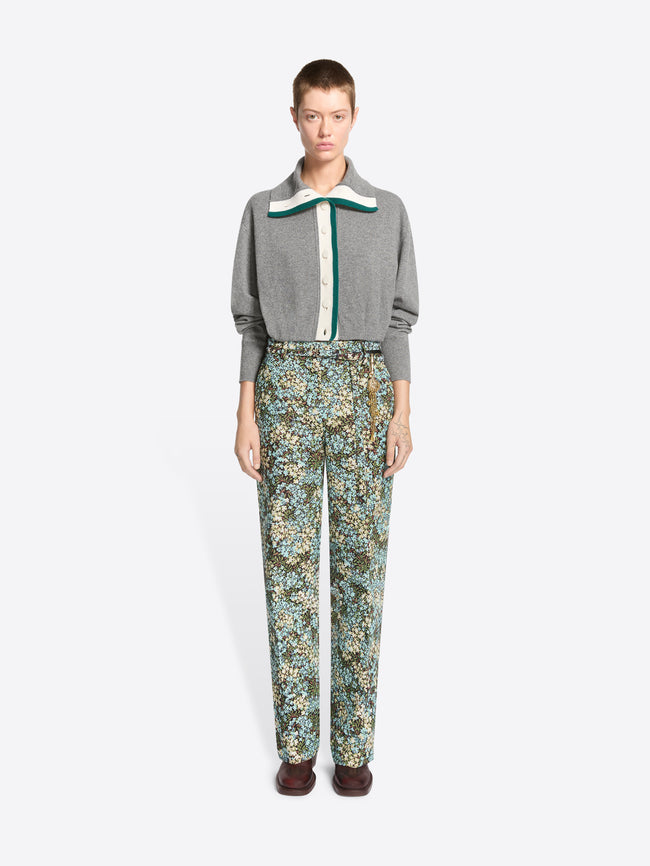 A model stands against a light gray background wearing a gray knit cardigan with a green and white collar detail, paired with high-waisted floral patterned pants and dark brown shoes.