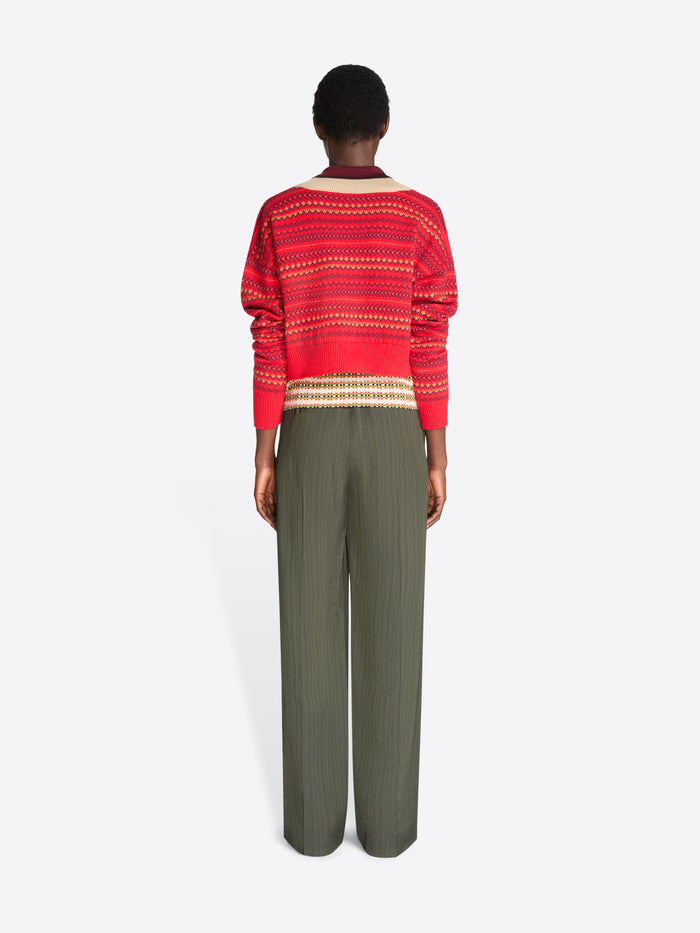 Back view of a model standing against a light gray background wearing a red and beige patterned knit sweater, paired with olive green wide-leg pants.