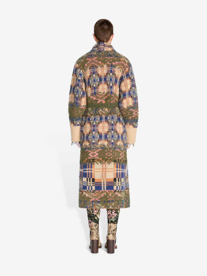 Back view of a model standing against a light gray background wearing a long patterned coat with a matching belt, paired with patterned tights and snakeskin heels.