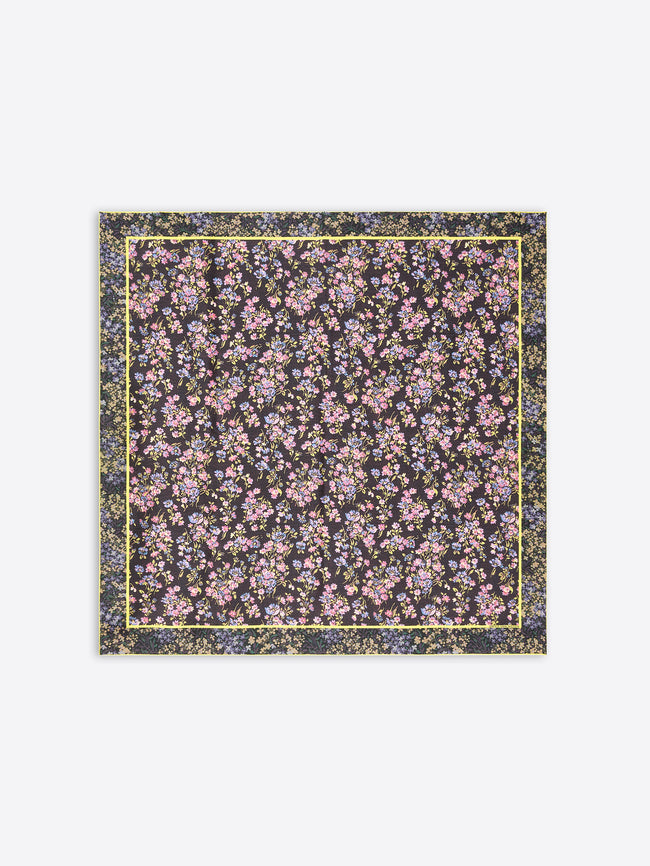 A square scarf featuring an all-over dense floral print  on a dark background, framed by a thin yellow border on a light gray background.