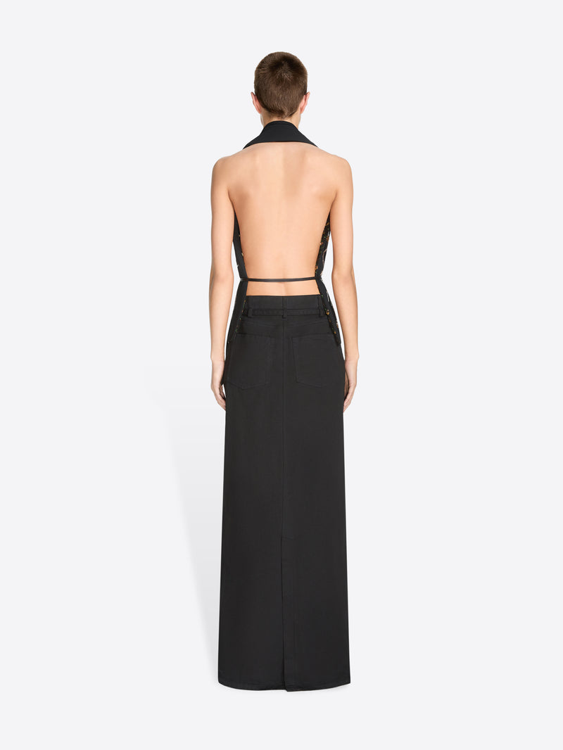 A model wearing a black sleeveless wrap-style top with a low open back paired with a long black skirt against a light gray background.