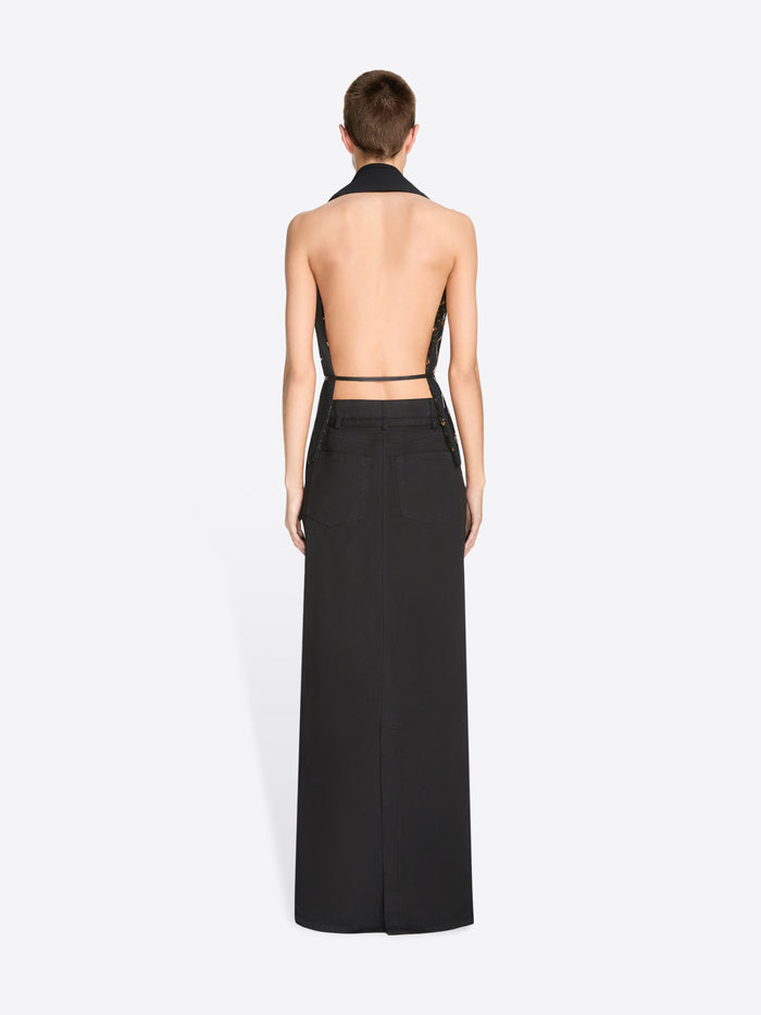 A model wearing a black sleeveless wrap-style top with a low open back paired with a long black skirt against a light gray background.
