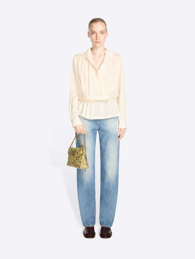 Full-length model wearing a cream striped blouse and light-wash jeans, carrying a small black-and-gold floral jacquard bag with green accents and chain handles.