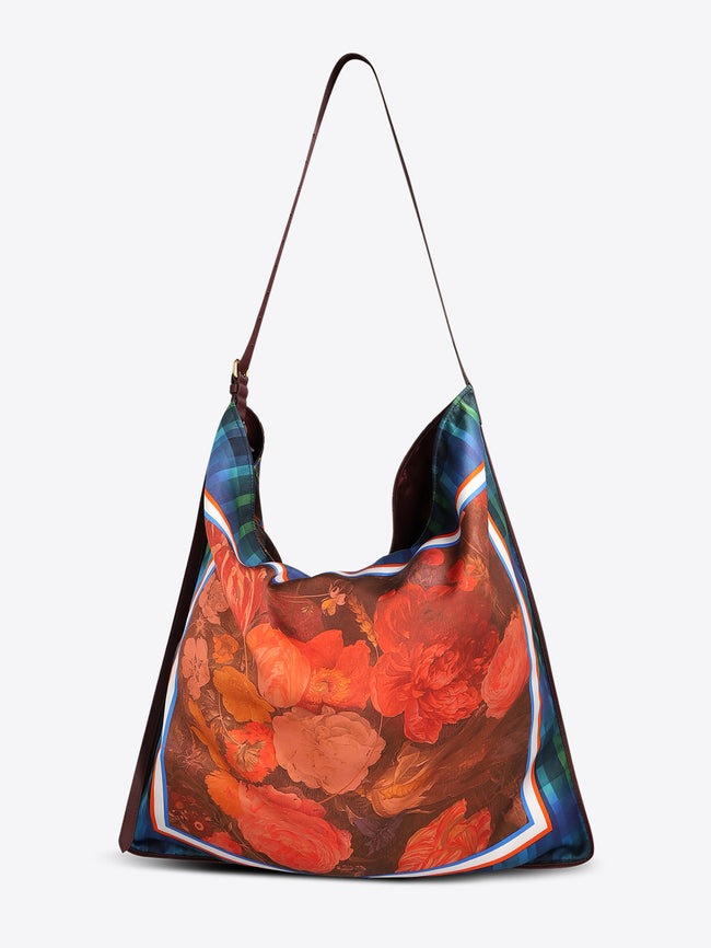 Triangular shoulder bag with a long dark brown strap, blue-green plaid panels, and a red-orange floral center framed with striped trim on a light gray background.