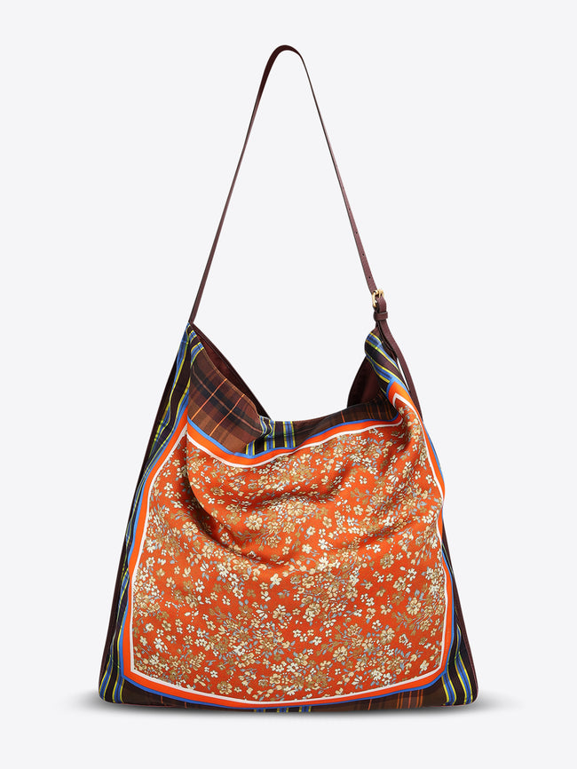Back view of a triangular shoulder bag with a long dark brown strap, brown plaid panels, and an orange floral center framed with striped trim on a light gray background.