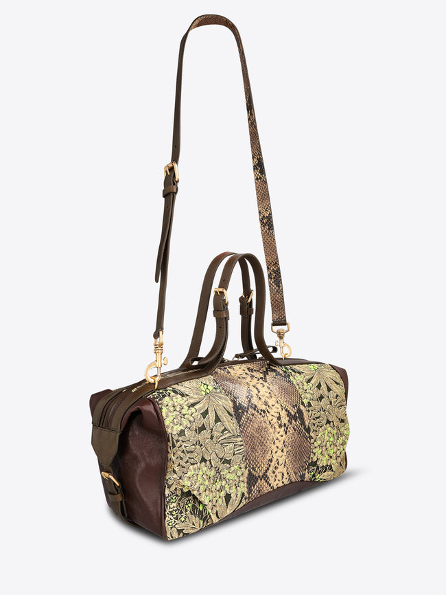 Structured duffle bag with dark brown leather trim, a tan snakeskin-effect center panel, and black-and-gold floral jacquard sides with green accents on a light gray background.