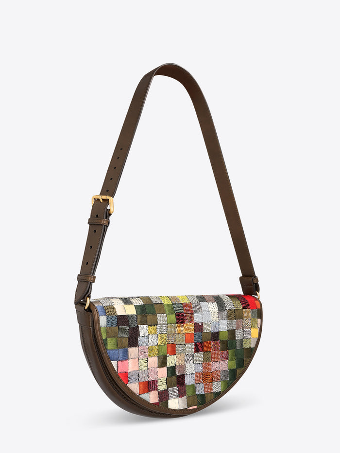 Half-moon shoulder bag with a dark brown leather strap and multicolored textured patchwork panel on a light gray background.