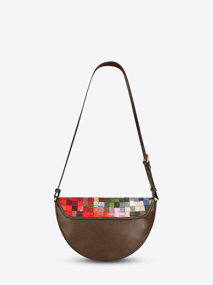 Back view of a half-moon shoulder bag with a dark brown leather strap and multicolored textured patchwork panel on a light gray background.