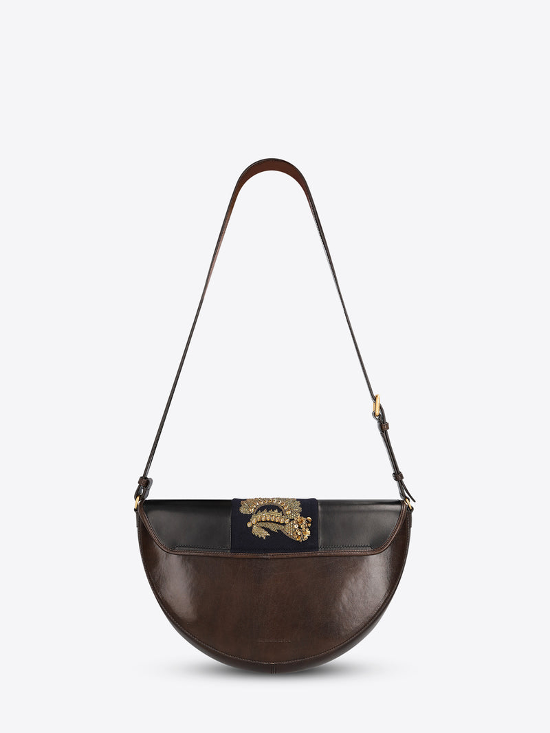 Back view of a leather half-moon shoulder bag with a dark brown strap and a navy center panel featuring ornate gold-toned embroidery and sequins on a light gray background.
