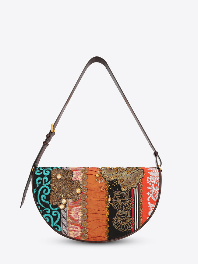 Half-moon shoulder bag with a dark brown leather strap and multicolored patchwork panels featuring embroidery, beading, and floral appliqués on a light gray background.