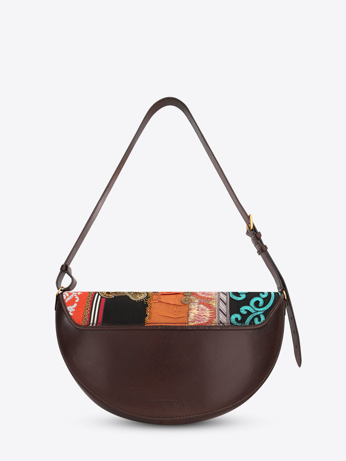 Back view of a half-moon shoulder bag with a dark brown leather strap and multicolored patchwork panels featuring embroidery, beading, and floral appliqués on a light gray background.