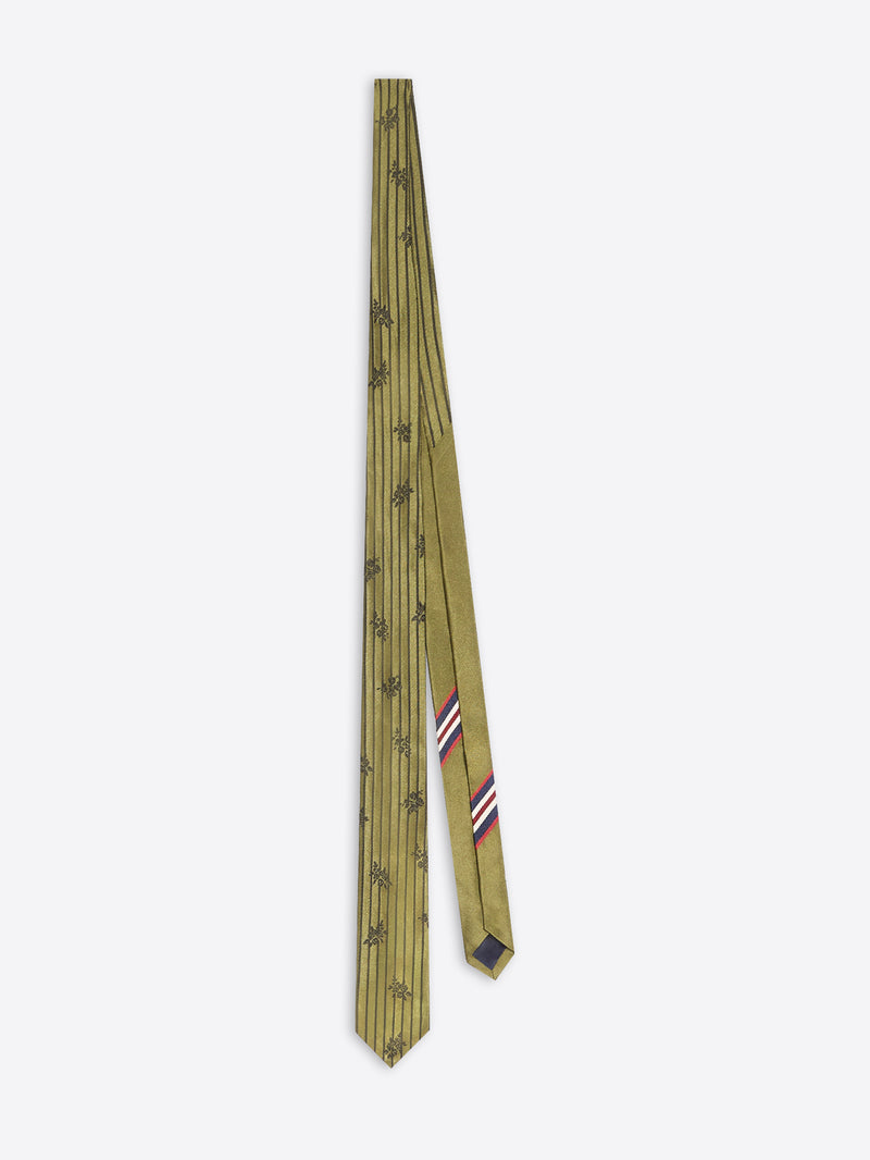 A tie in olive green with a repeating pattern and a small striped accent in red, white, and blue near the tip, displayed on a light gray background.