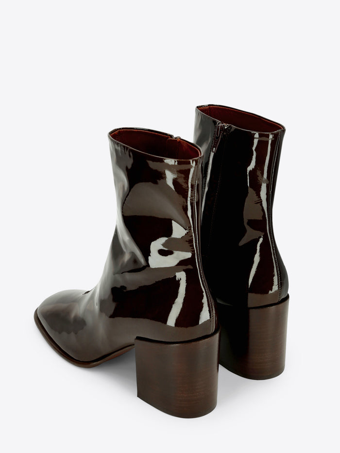 A pair of dark olive patent leather ankle boots with a rounded square toe and chunky block heel on a light gray background.