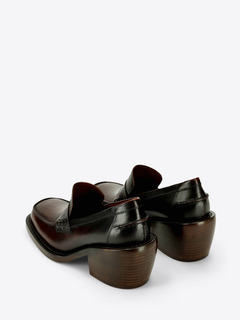 Dark brown leather penny loafer with a raised tongue, square moc toe, and chunky stacked block heel on a light gray background.