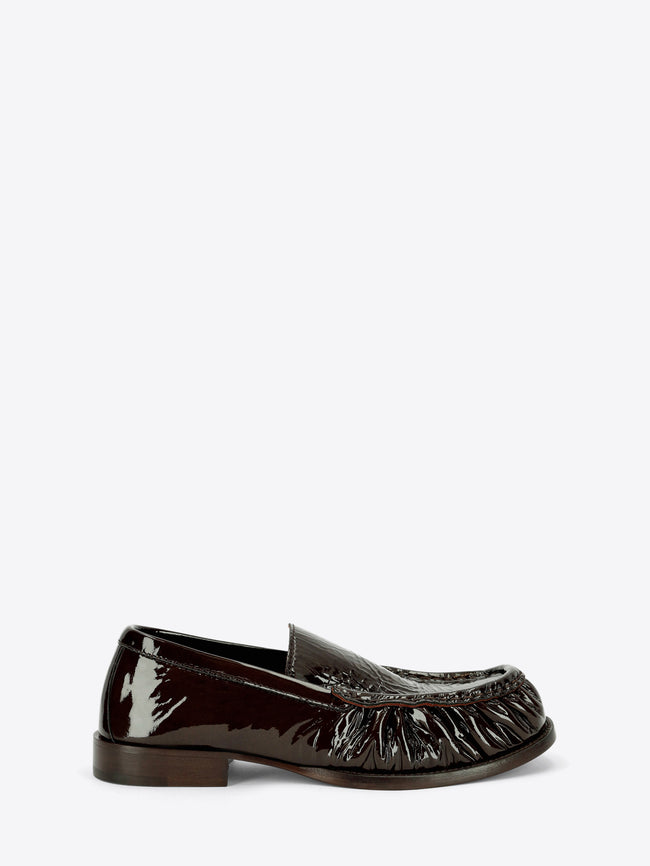 Dark brown patent leather loafer with gathered detailing around the rounded toe and a low stacked heel on a light gray background.
