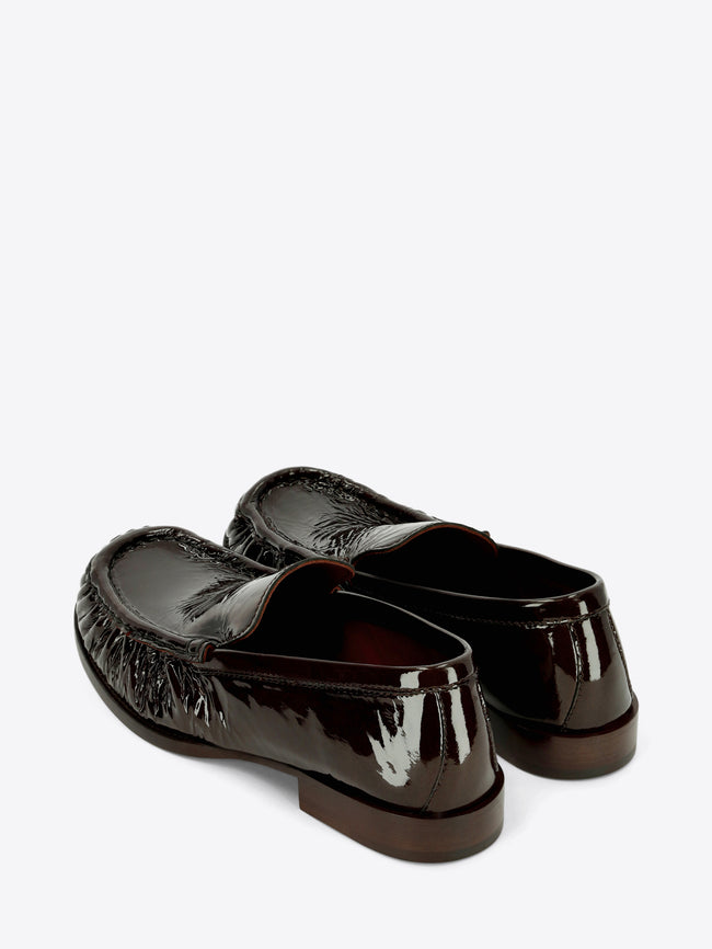Dark brown patent leather loafers with gathered detailing around the rounded toe and a low stacked heel on a light gray background.