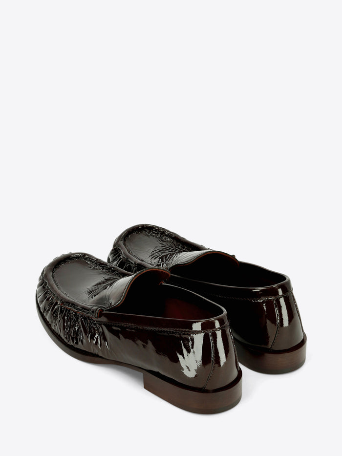 Dark brown patent leather loafers with gathered detailing around the rounded toe and a low stacked heel on a light gray background.
