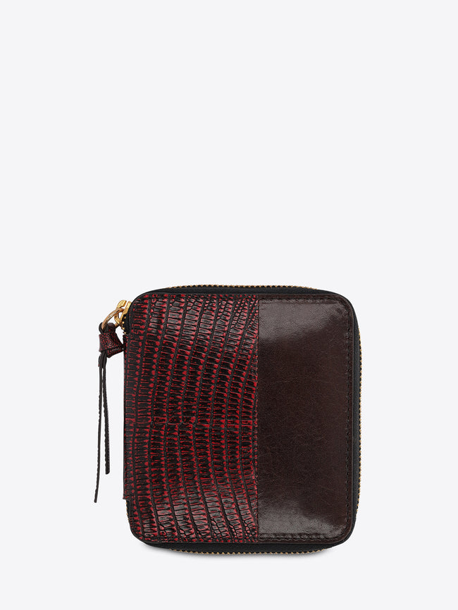 A small zip-around wallet with a split design: one side features a red and black crocodile-embossed texture, and the other side is smooth dark brown on the light gray background. 