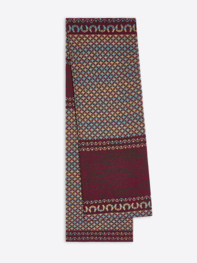 A folded patterned scarf in deep burgundy, beige and blue, featuring geometric and wavy border designs, shown against a light gray background.