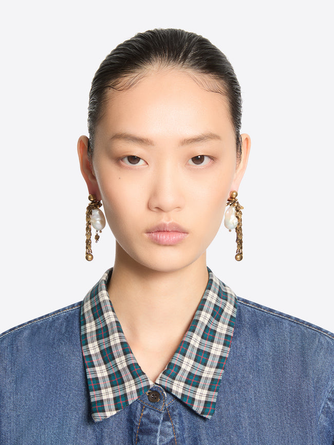 Pair of old brass drop earrings with irregular white pearl pendants, cascading leaf-shaped links, and spherical charms, worn by a model.