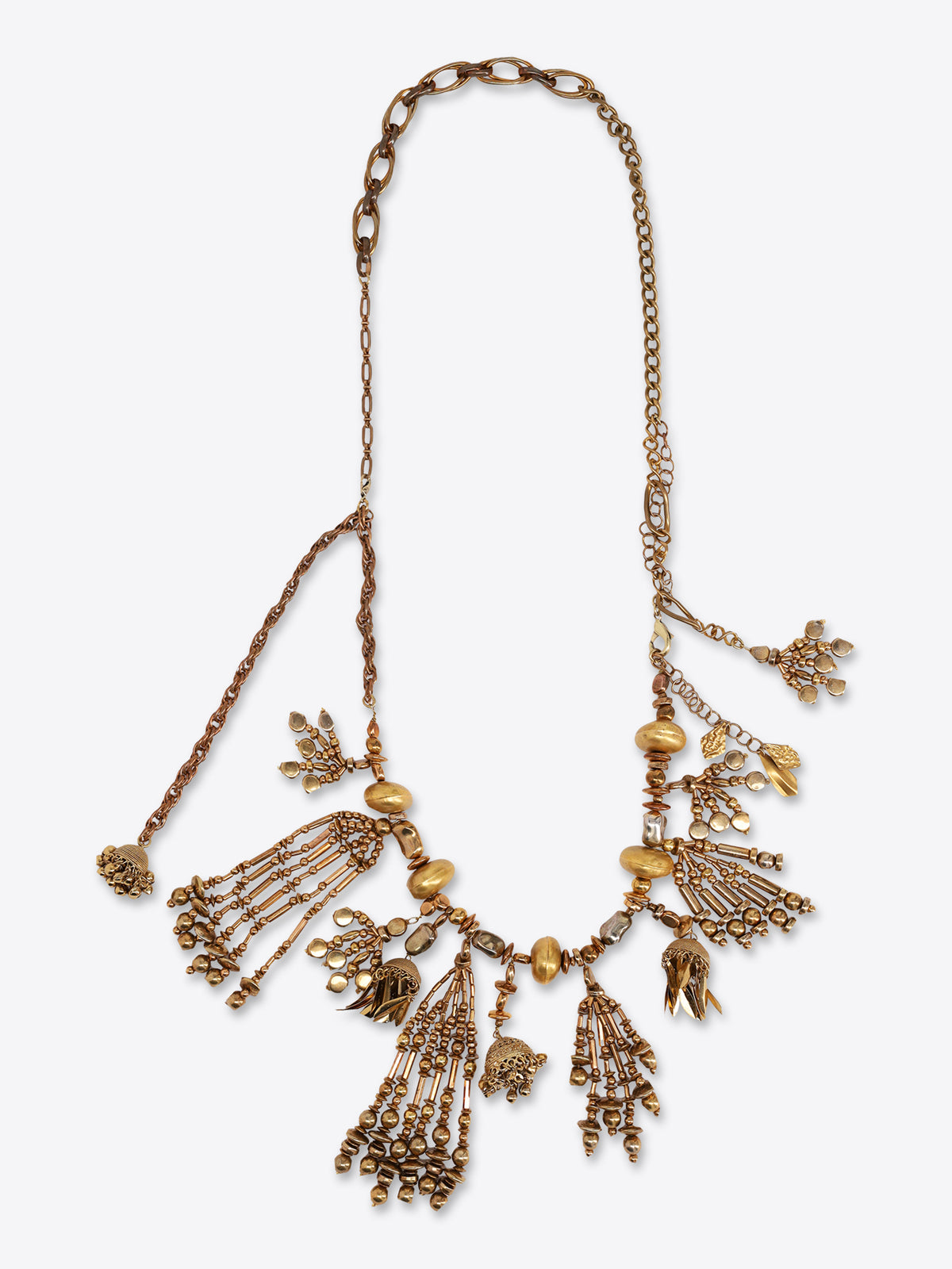 Old brass necklace with mixed chain links, sculpted beads, and multiple dangling tassel and floral charms on a light gray background.