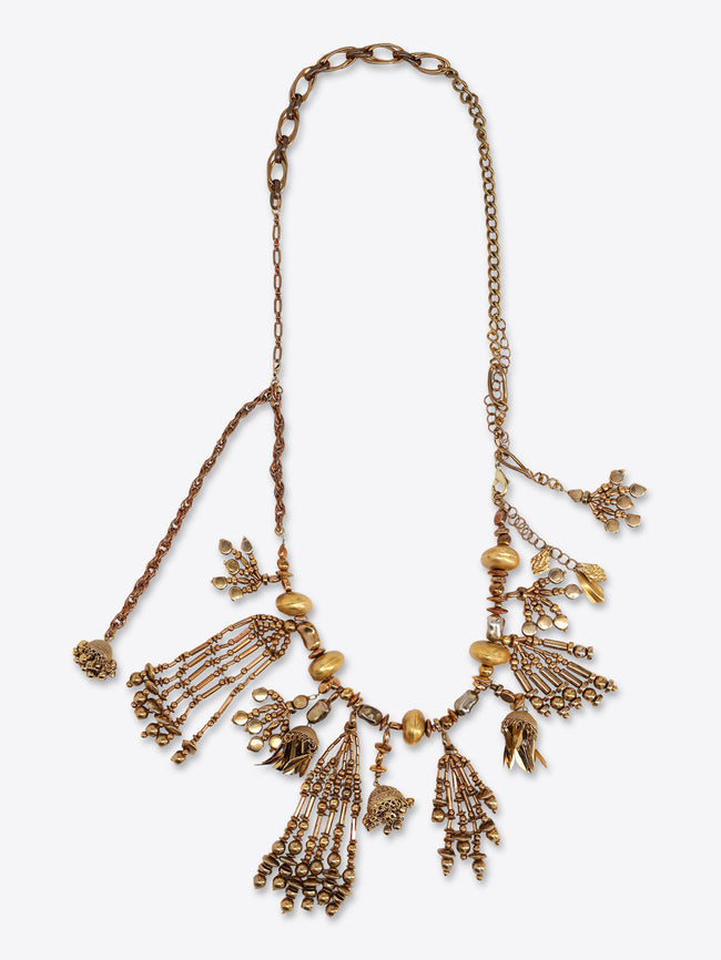 Old brass necklace with mixed chain links, sculpted beads, and multiple dangling tassel and floral charms on a light gray background.