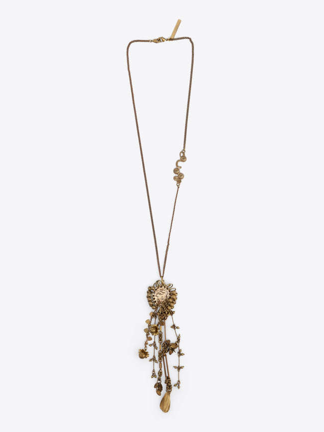 Long old brass necklace with an embossed medallion pendant and cascading floral, bead, and teardrop charms on a light gray background.