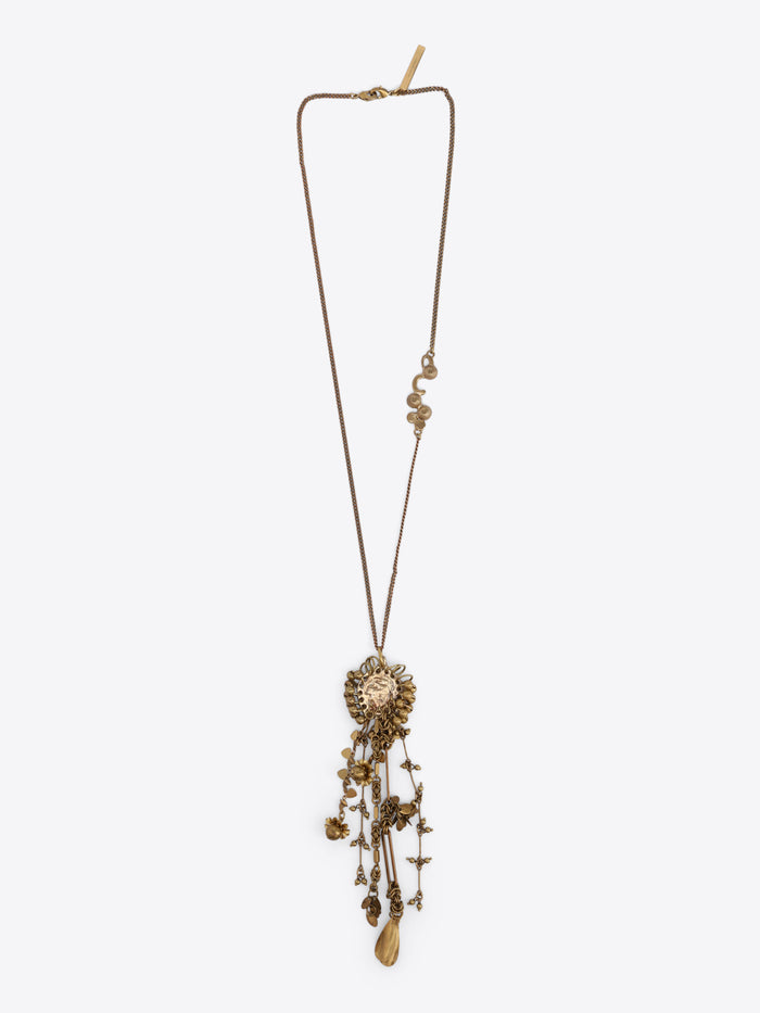 Long old brass necklace with an embossed medallion pendant and cascading floral, bead, and teardrop charms on a light gray background.