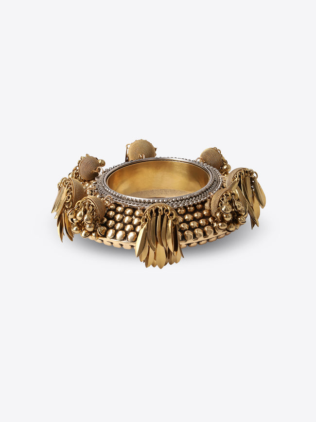 Ornate old brass cuff bracelet with a textured beaded surface, silver-toned edging, and dangling leaf and bead charms on a light gray background.